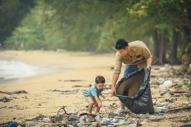 Vater und Kind sammeln Plastik am Strand - Meeresverschmutzung